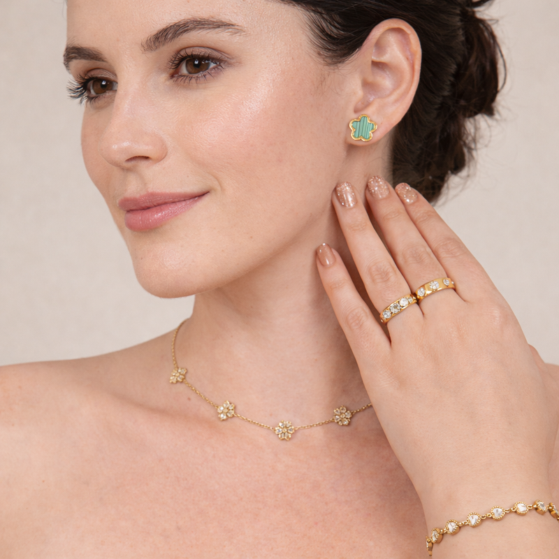 Woman wearing a gold floral necklace, green clover stud earrings, gold ring, and gold bracelet in a minimal jewelry lifestyle image