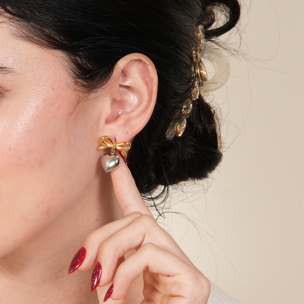 Bow-on-heart stud earrings in 18K gold plating with enamel finish, designed for women in the UAE who love playful elegance with a premium touch.