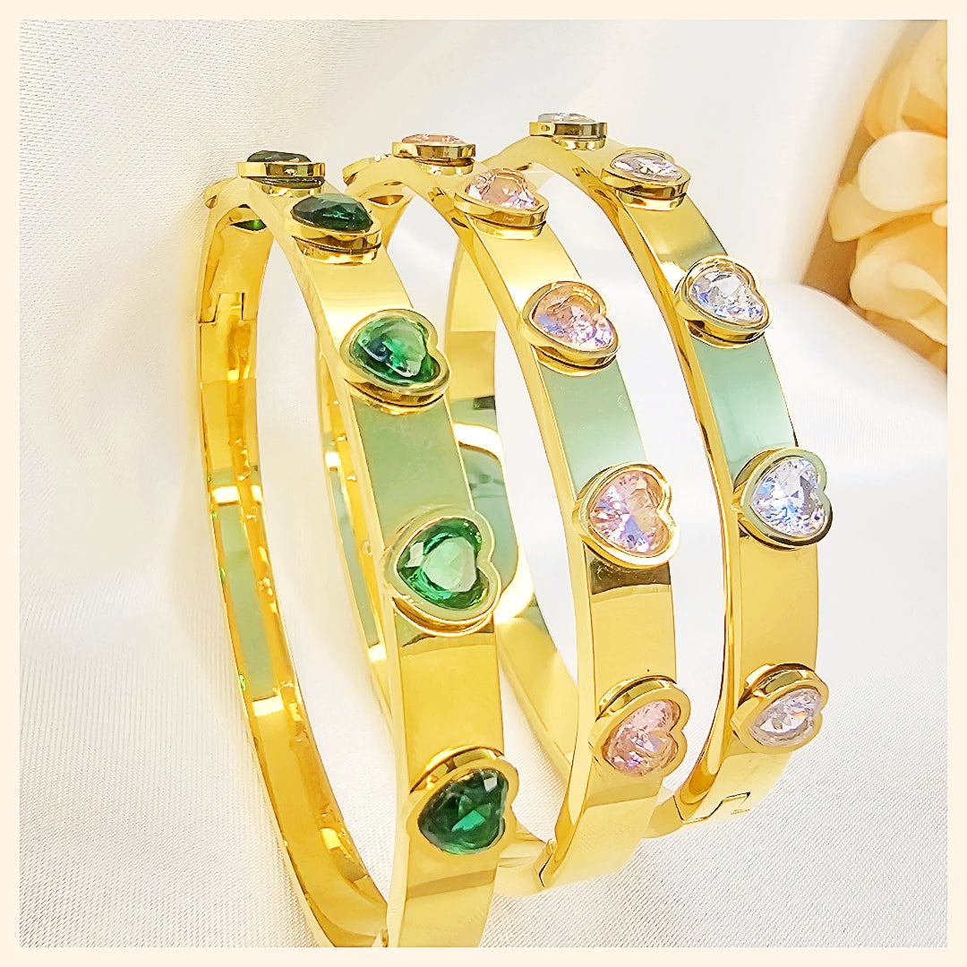 Gold bangles with green and pink gemstones on a light background