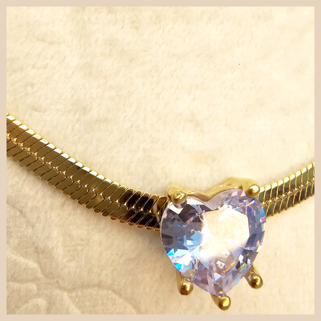 Gold necklace with a heart-shaped clear gemstone on a beige background
