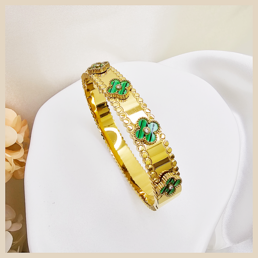 Gold bracelet with green gemstones on a white cushion