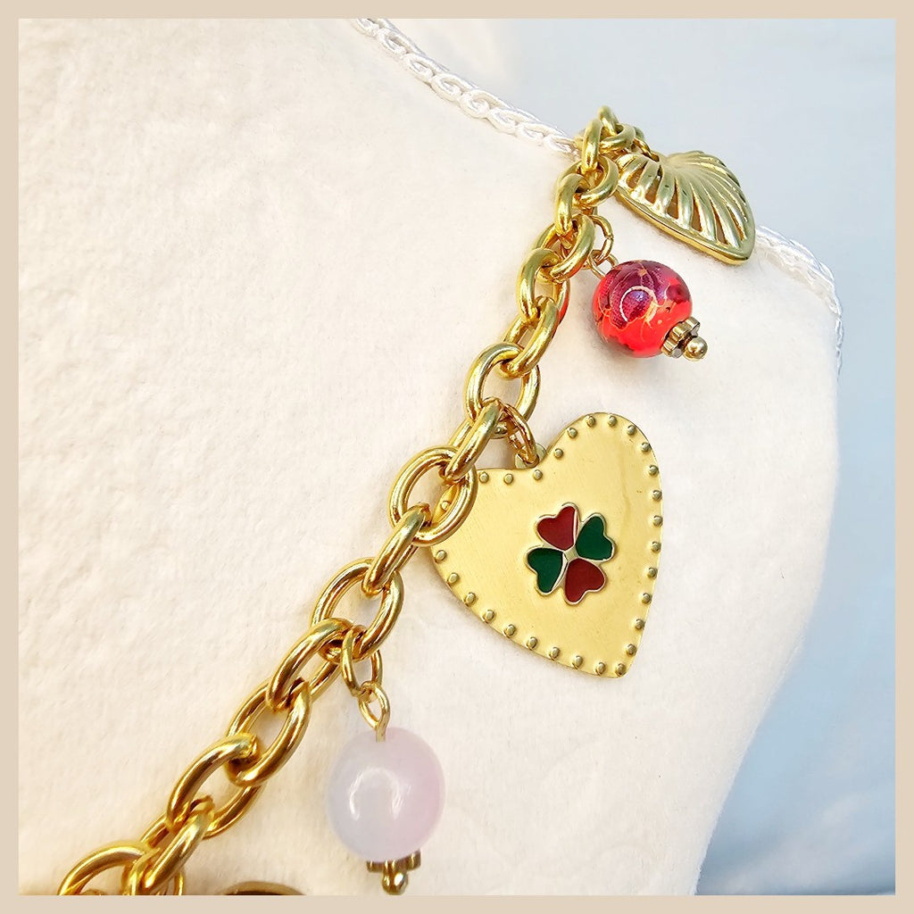 Gold chain bracelet with heart-shaped charm and colorful beads on a white cushion.