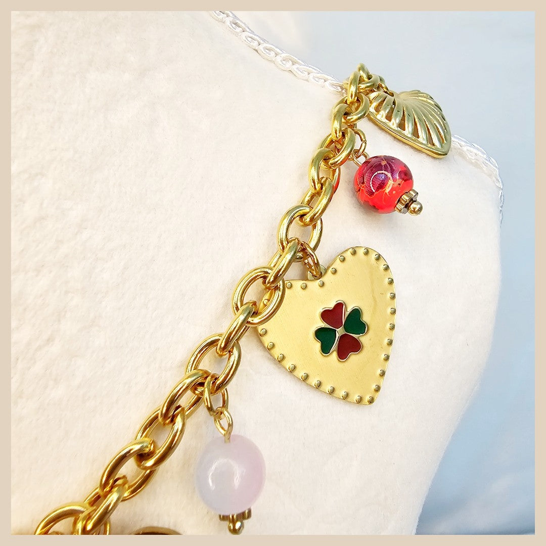 Gold chain bracelet with heart-shaped charm and colorful beads on a white cushion.