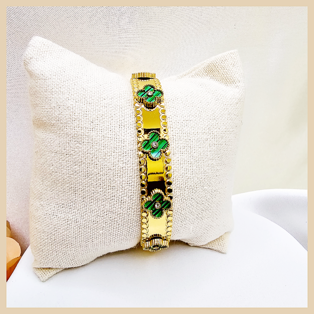 Gold bracelet with green stones on a white pillow