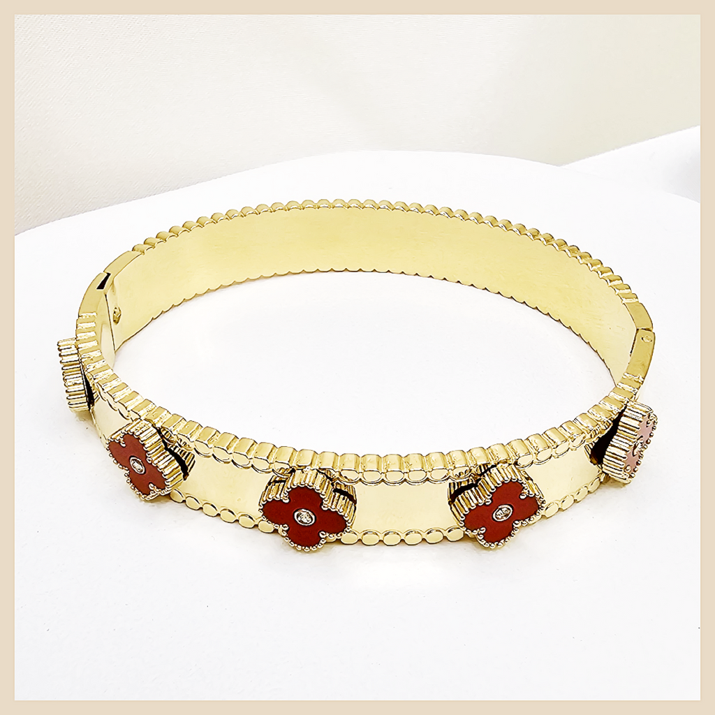 Gold bracelet with red flower-shaped stones on a light beige background
