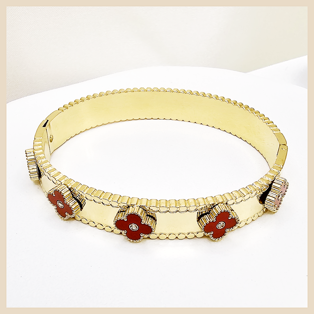 Gold bracelet with red flower-shaped stones on a light beige background